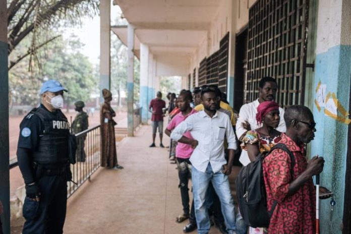 Des électeurs font la queue devant un bureau de vote de Bangui, sous l'oeil d'un policier de la Minusca, le 27 décembre 2020 afp.com - ALEXIS HUGUET
